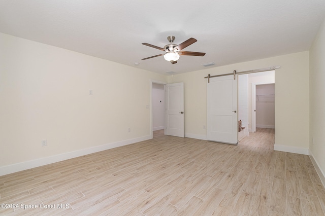 unfurnished bedroom featuring a closet, a spacious closet, a barn door, light hardwood / wood-style floors, and ceiling fan