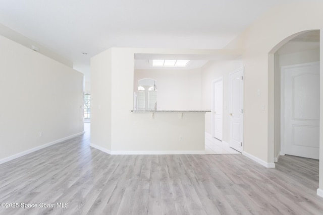 unfurnished room featuring light wood-style floors, arched walkways, and baseboards