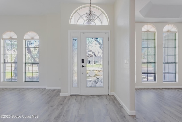 foyer entrance featuring baseboards, light wood-style flooring, a wealth of natural light, and an inviting chandelier