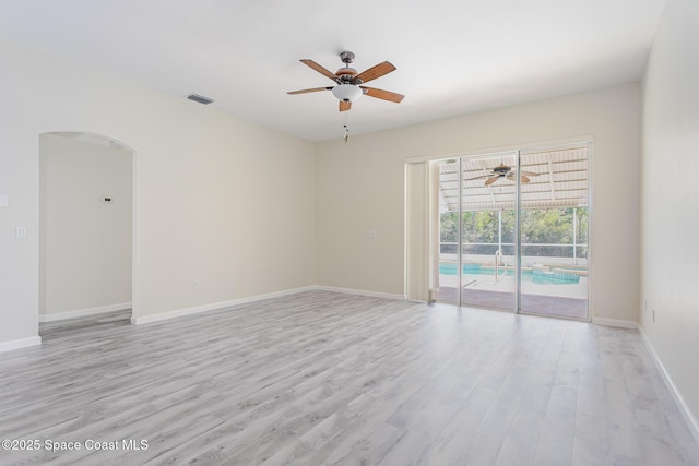 empty room featuring arched walkways, a ceiling fan, light wood-style flooring, and baseboards