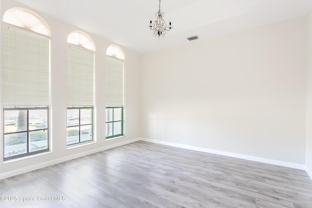 unfurnished room with light wood-style floors, visible vents, baseboards, and a chandelier