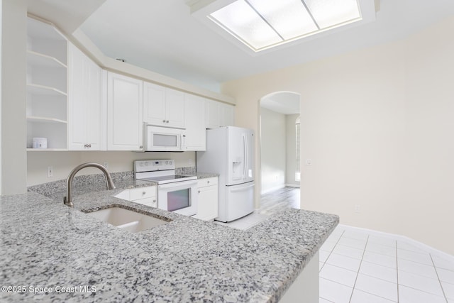 kitchen featuring arched walkways, white appliances, a sink, light stone countertops, and open shelves