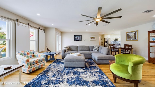 living room with a barn door, ceiling fan, and light wood-type flooring