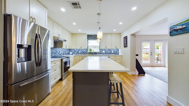 kitchen with a center island, stainless steel appliances, hanging light fixtures, a breakfast bar, and light hardwood / wood-style flooring