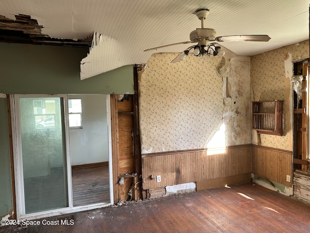 empty room with wooden walls, wainscoting, ceiling fan, and hardwood / wood-style floors