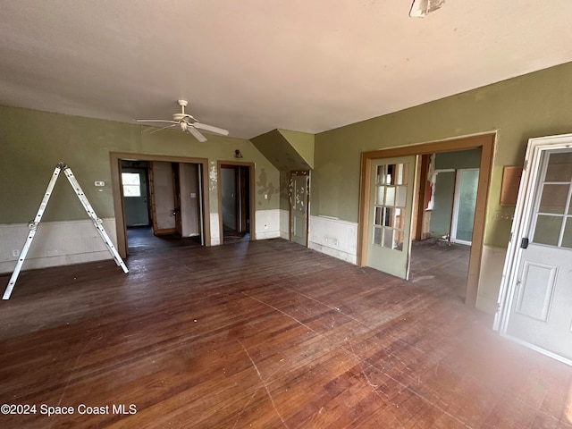 unfurnished living room with hardwood / wood-style floors, lofted ceiling, ceiling fan, and wainscoting