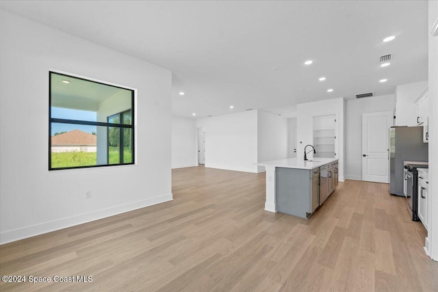 kitchen with light hardwood / wood-style floors, a center island with sink, stainless steel range with electric stovetop, sink, and white cabinetry