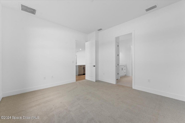 unfurnished bedroom featuring light carpet, connected bathroom, and baseboards