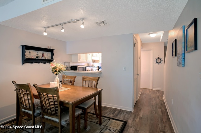 dining space featuring rail lighting, dark wood-type flooring, and a textured ceiling