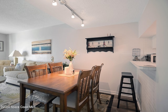 dining room with a textured ceiling, dark hardwood / wood-style floors, and rail lighting