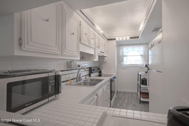 kitchen featuring tile countertops, white cabinets, sink, light hardwood / wood-style flooring, and appliances with stainless steel finishes