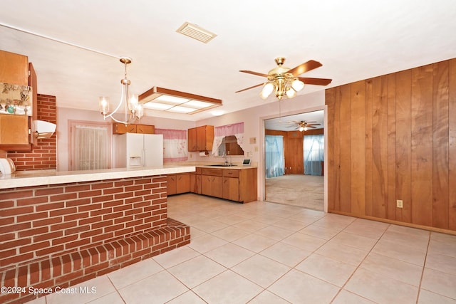 kitchen featuring sink, wooden walls, white fridge with ice dispenser, decorative light fixtures, and kitchen peninsula