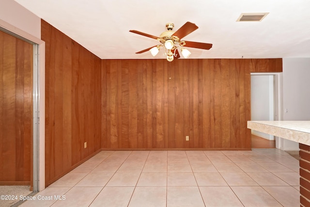 spare room with ceiling fan, light tile patterned flooring, and wooden walls