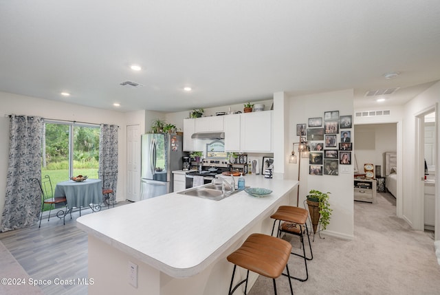 kitchen featuring white cabinetry, appliances with stainless steel finishes, a breakfast bar area, kitchen peninsula, and light colored carpet