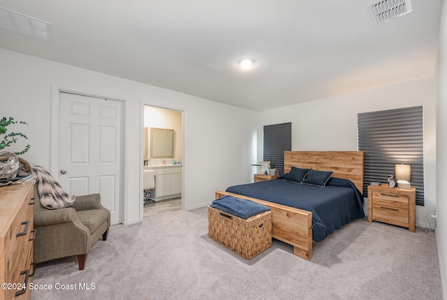 bedroom featuring a textured ceiling, light colored carpet, and ensuite bathroom