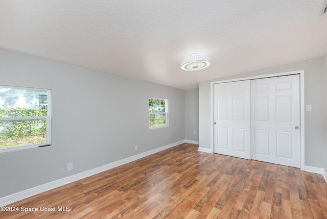 unfurnished bedroom featuring a textured ceiling, a closet, hardwood / wood-style floors, and lofted ceiling