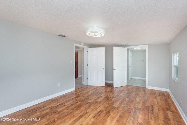 unfurnished bedroom featuring wood-type flooring, a textured ceiling, and a spacious closet