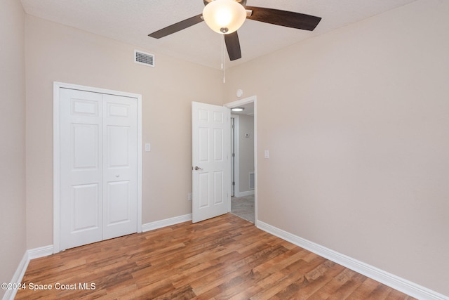 unfurnished bedroom featuring ceiling fan, a closet, a textured ceiling, and hardwood / wood-style flooring