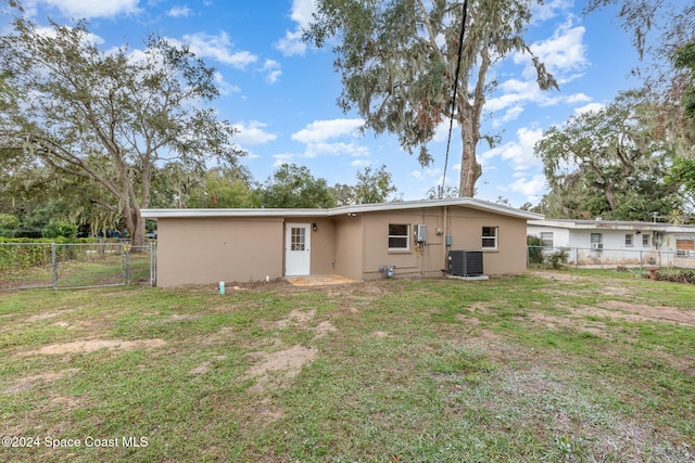 rear view of house with central AC unit and a lawn