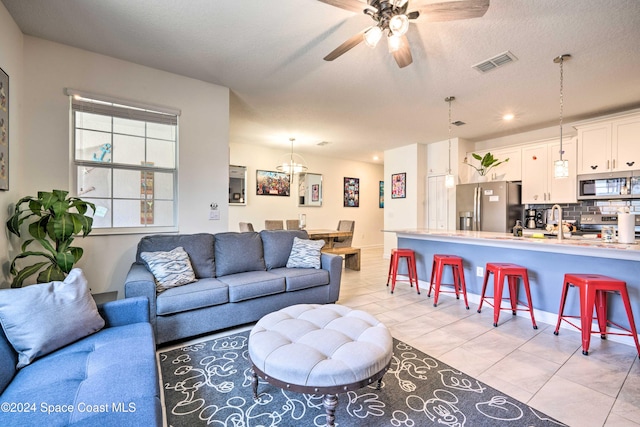 living room with a textured ceiling, light tile patterned floors, ceiling fan, and sink