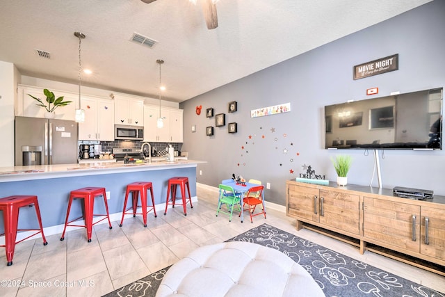 kitchen with stainless steel appliances, a kitchen breakfast bar, a textured ceiling, hanging light fixtures, and decorative backsplash