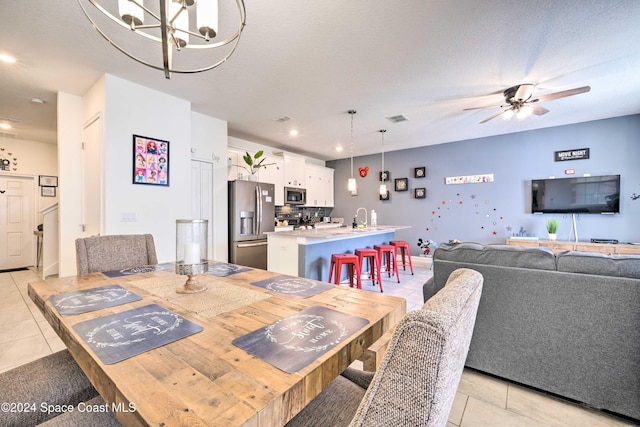 dining area with ceiling fan with notable chandelier, a textured ceiling, light tile patterned floors, and sink