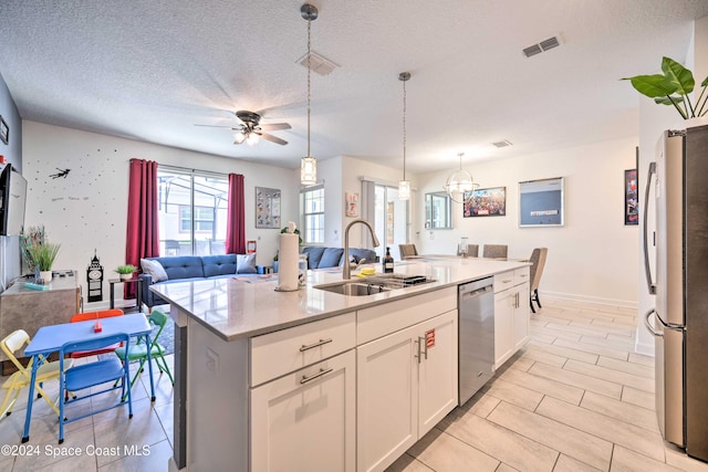 kitchen with stainless steel appliances, white cabinetry, a textured ceiling, sink, and an island with sink