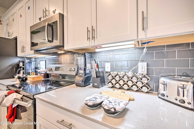 kitchen featuring white cabinetry, decorative backsplash, appliances with stainless steel finishes, and light stone counters