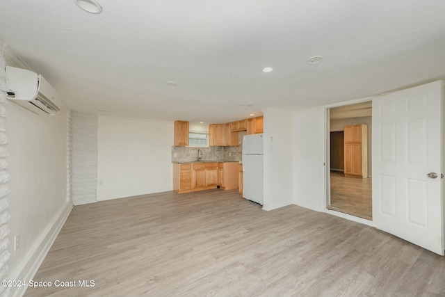 unfurnished living room with a wall mounted AC, sink, and light wood-type flooring