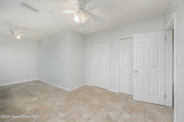 unfurnished bedroom featuring ceiling fan, light tile patterned floors, and two closets