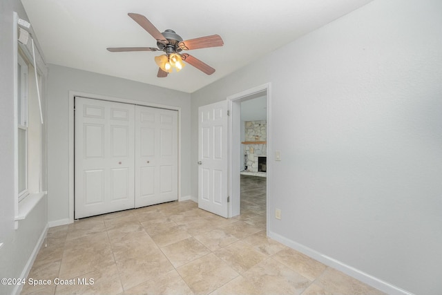 unfurnished bedroom with light tile patterned flooring, a stone fireplace, a closet, and ceiling fan