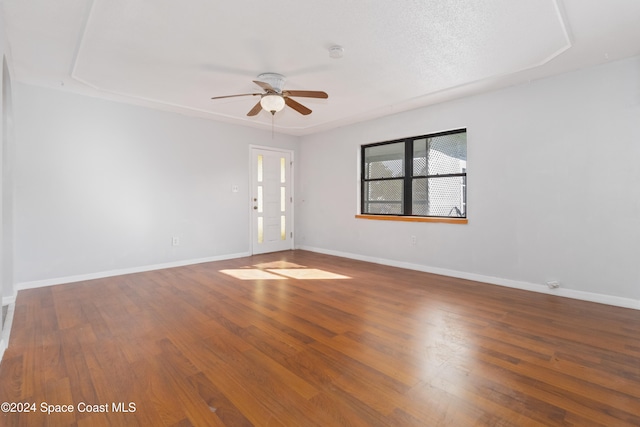 empty room with hardwood / wood-style floors, ceiling fan, and a raised ceiling