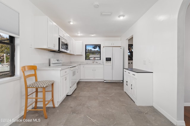 kitchen featuring white cabinets, white appliances, sink, and a wealth of natural light