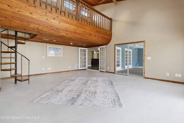 unfurnished living room with concrete flooring, french doors, wooden ceiling, and a towering ceiling