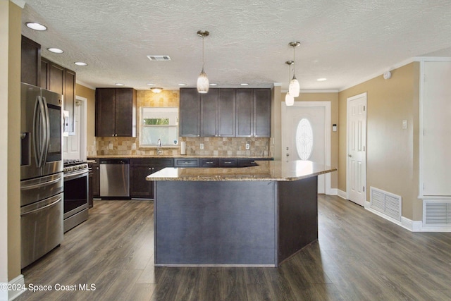 kitchen featuring appliances with stainless steel finishes, a textured ceiling, hanging light fixtures, a kitchen island, and dark wood-type flooring