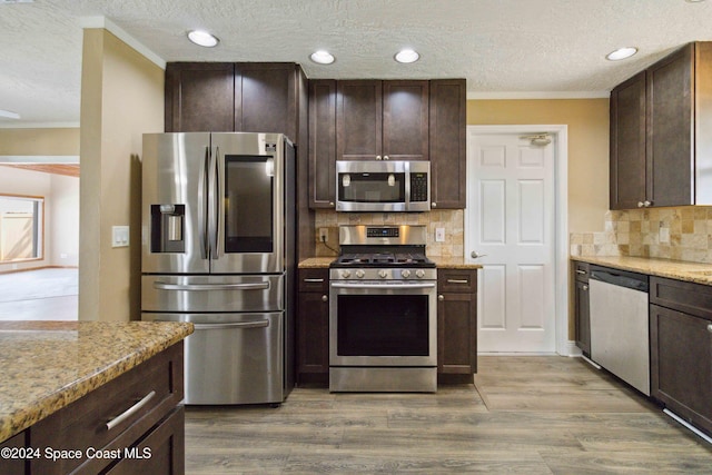 kitchen with hardwood / wood-style flooring, appliances with stainless steel finishes, light stone countertops, crown molding, and decorative backsplash