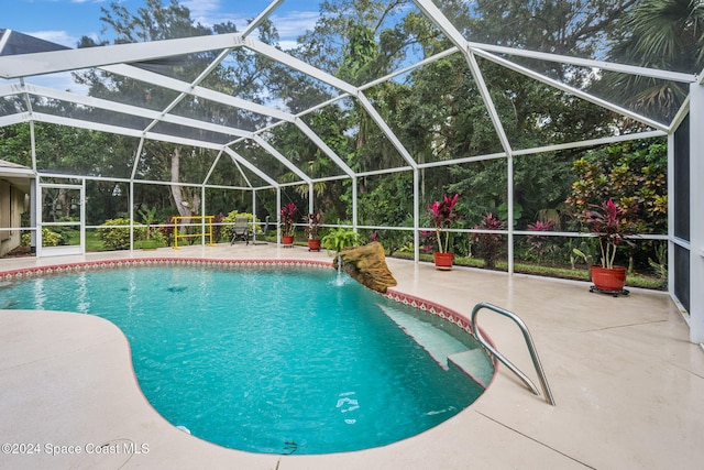 view of pool featuring glass enclosure, pool water feature, and a patio area