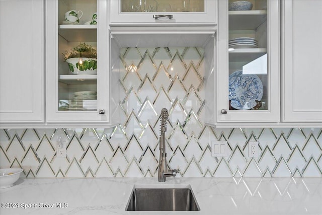 kitchen with white cabinets, decorative backsplash, sink, and light stone countertops