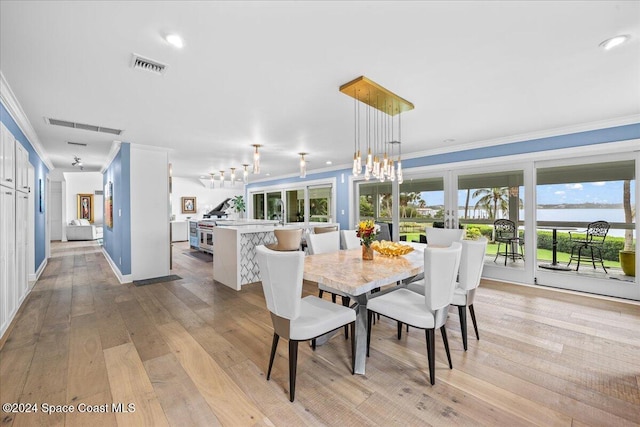 dining space with ornamental molding, light hardwood / wood-style floors, and a water view