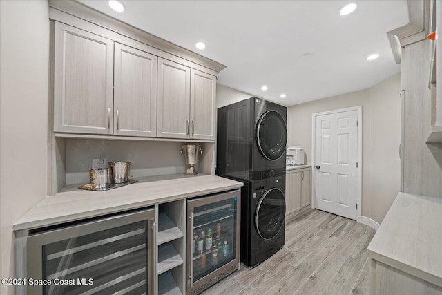 laundry area featuring cabinets, stacked washing maching and dryer, beverage cooler, and light hardwood / wood-style floors