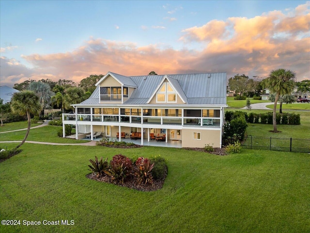 back house at dusk featuring a lawn, a patio, and a balcony