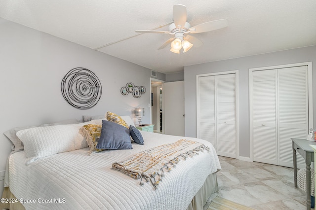 bedroom featuring a textured ceiling, ceiling fan, and two closets