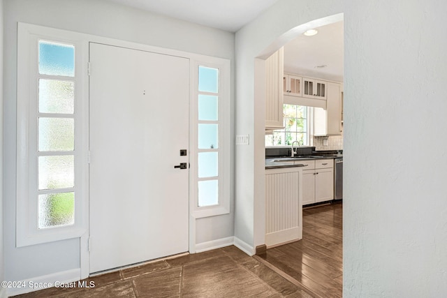 entrance foyer featuring arched walkways, baseboards, and dark wood-style flooring