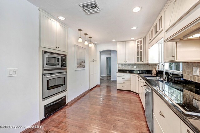 kitchen featuring visible vents, a sink, backsplash, stainless steel appliances, and arched walkways