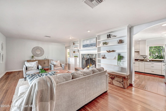 living area featuring visible vents, arched walkways, baseboards, and light wood finished floors