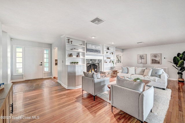 living area with a fireplace, visible vents, light wood-type flooring, and baseboards
