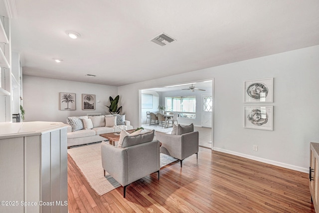 living area featuring ceiling fan, light wood-style floors, visible vents, and baseboards