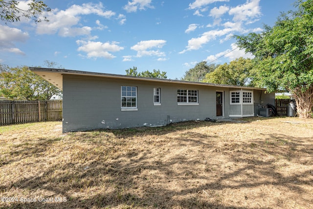 rear view of house featuring central AC unit and a lawn