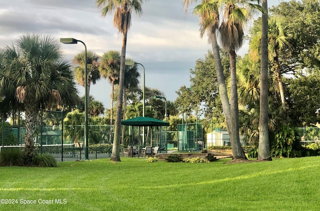 view of community featuring tennis court and a yard