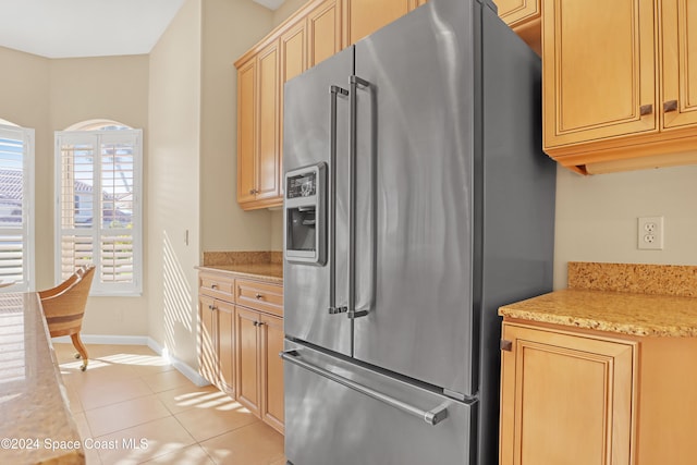 kitchen with light brown cabinetry, light tile patterned floors, light stone counters, and stainless steel fridge